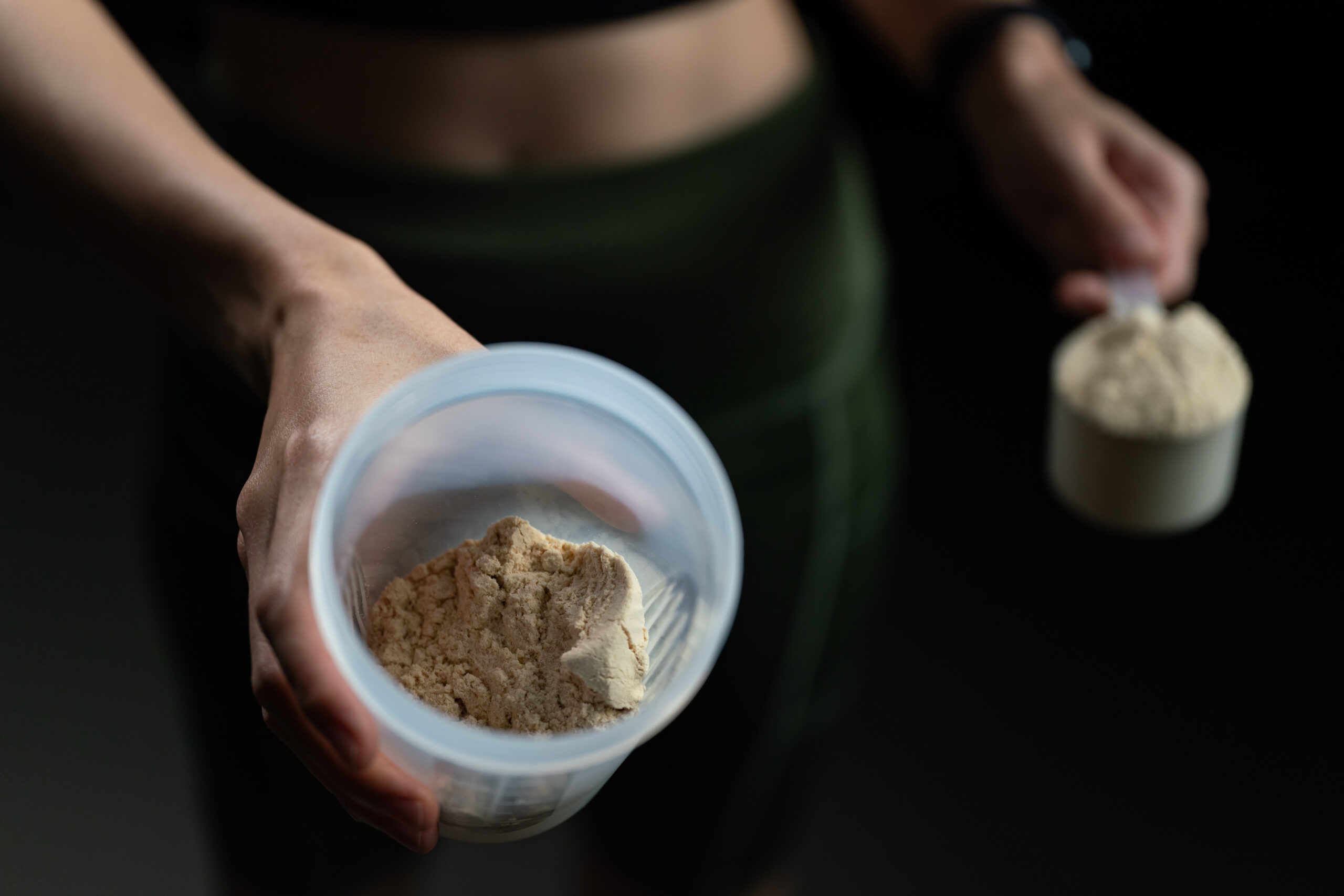 close up of women with measuring scoop of whey protein, jar and